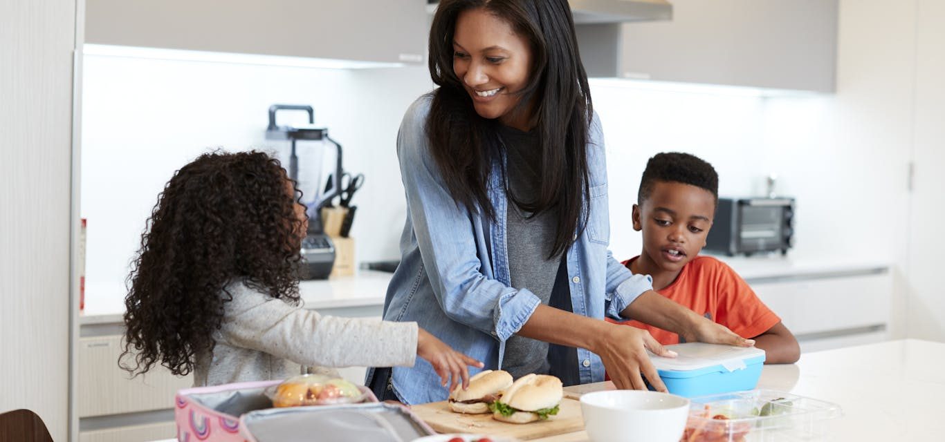 A mother and two children packing school lunches together in a warm kitchen